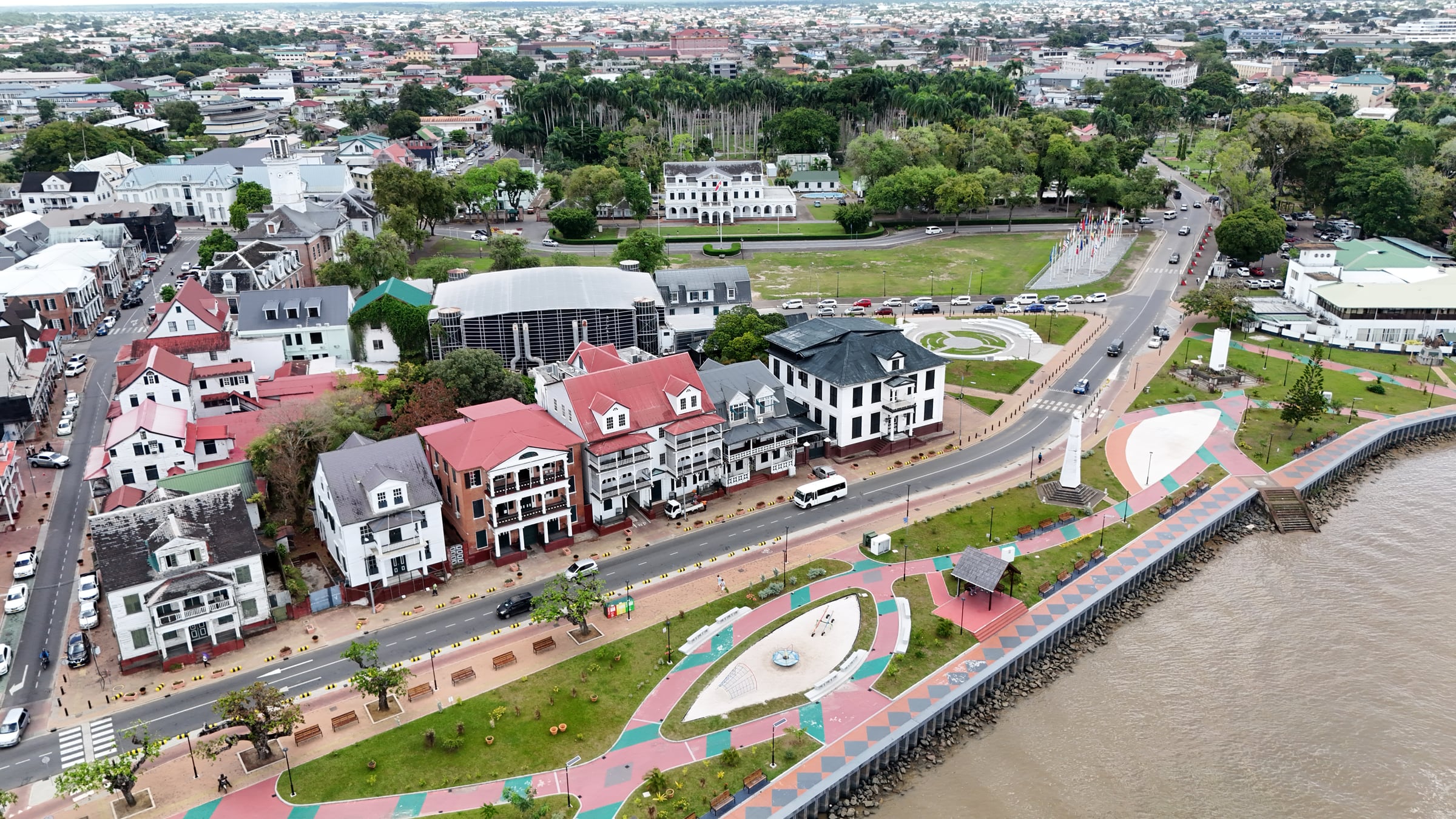 Luchtopname van de Waterkant in Paramaribo: de historische gevelrij, het park langs de rivier en het centrum daarachter